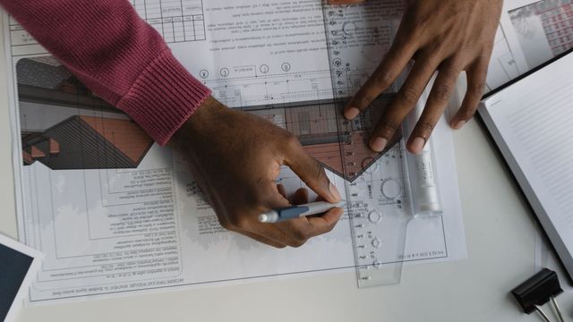 Photo : deux mains tracent un plan à la règle sur une table de travail