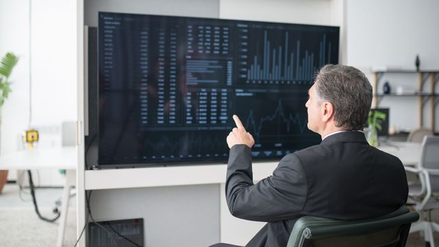 Photo : un consultant montre du doigt des indicateurs affichés sur un grand écran