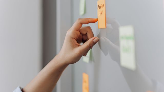Photo : une main colle une note sur un tableau de planification