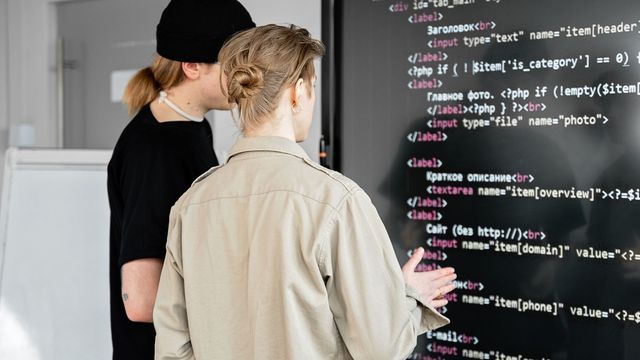 Photo : deux personnes relisent du code affiché sur un grand écran