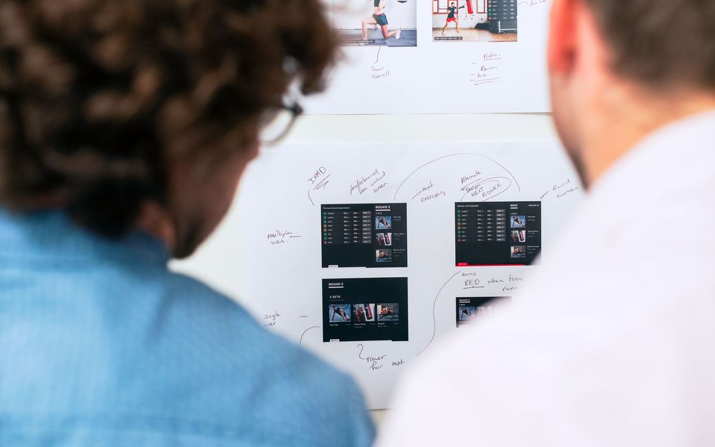 Photo : deux consultants examinent les maquettes d’une application affichées au mur